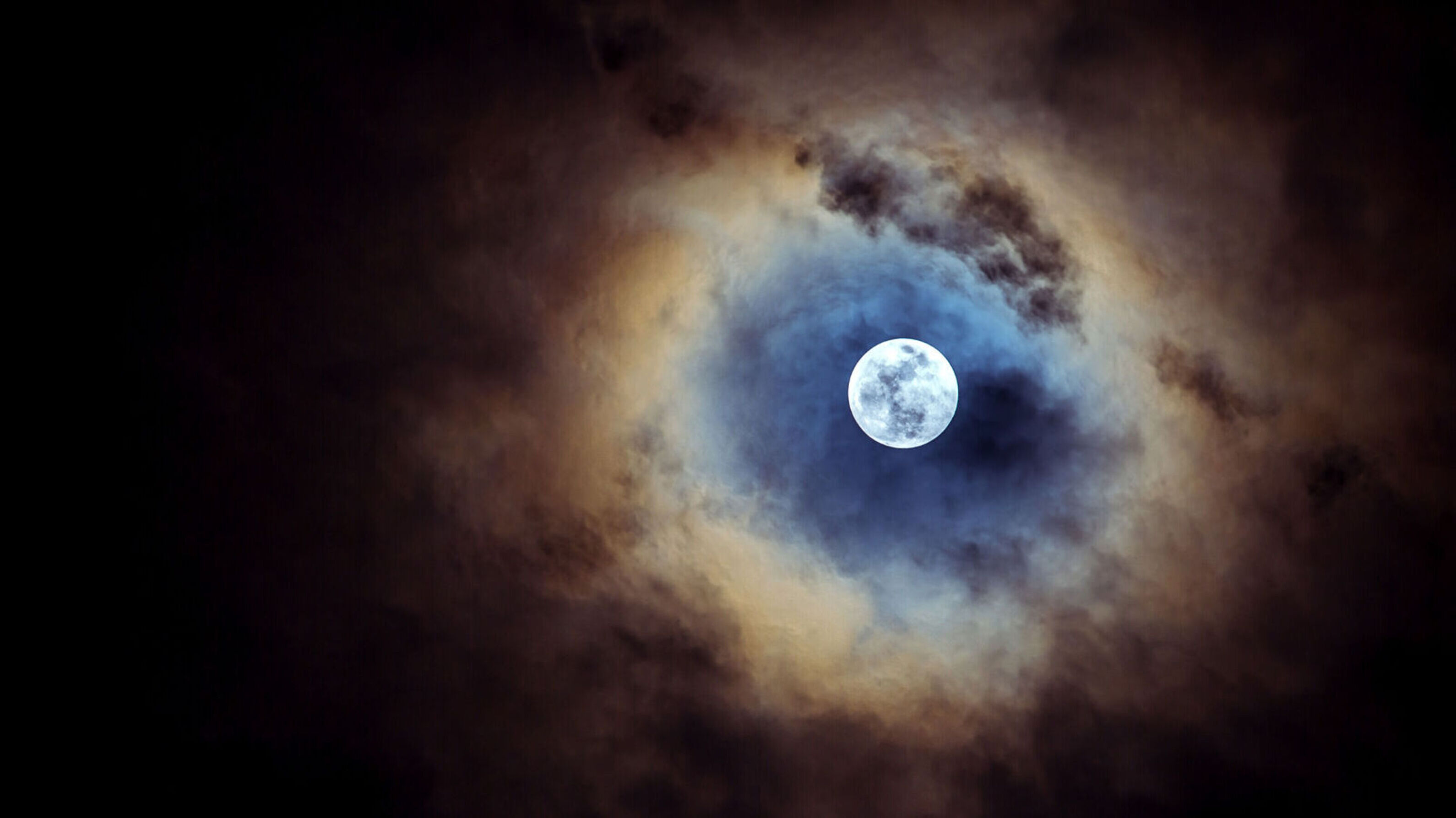 Full moon in black sky, partially covered by clouds