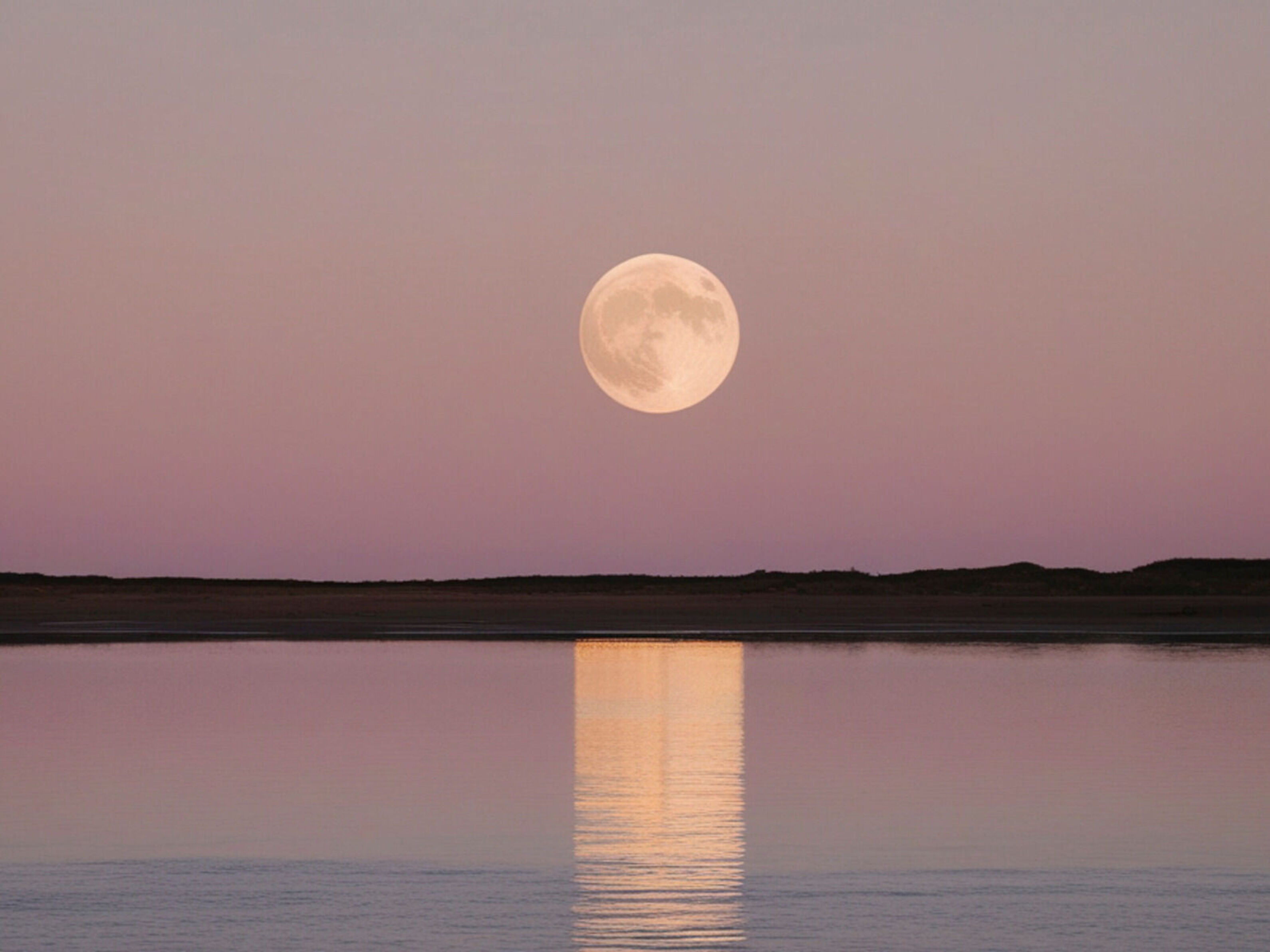 Full moon in the sky over a lake at dawn