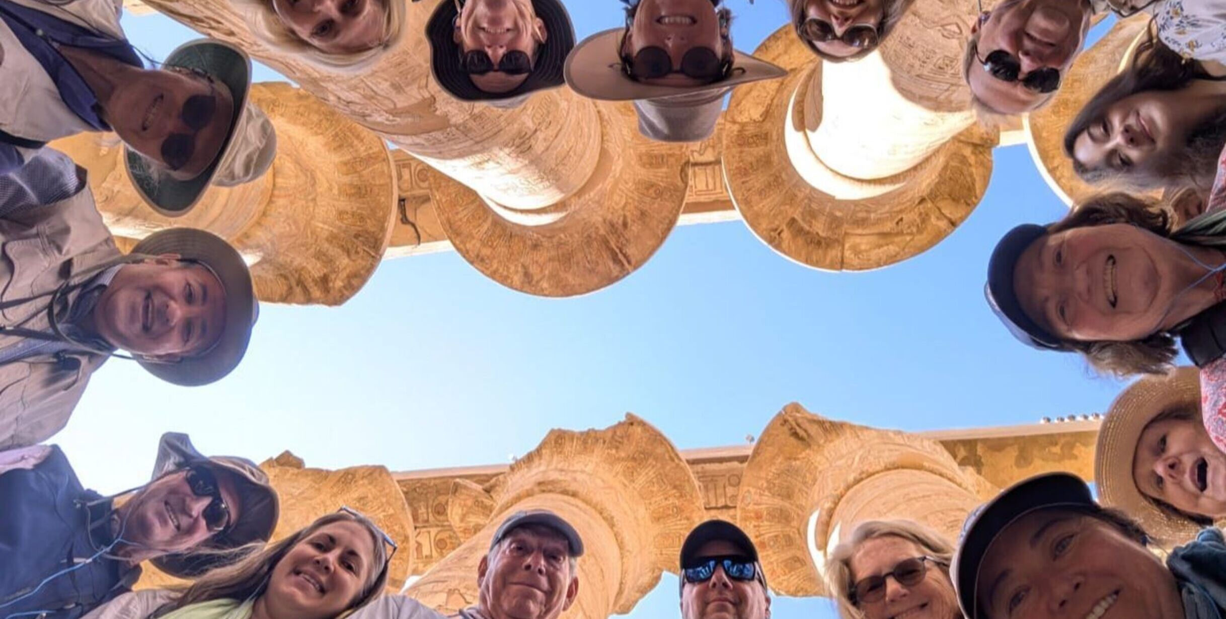 Picture of people with their heads peaking into edge of frame in the foreground with Egyptian ruins above and behind them in background